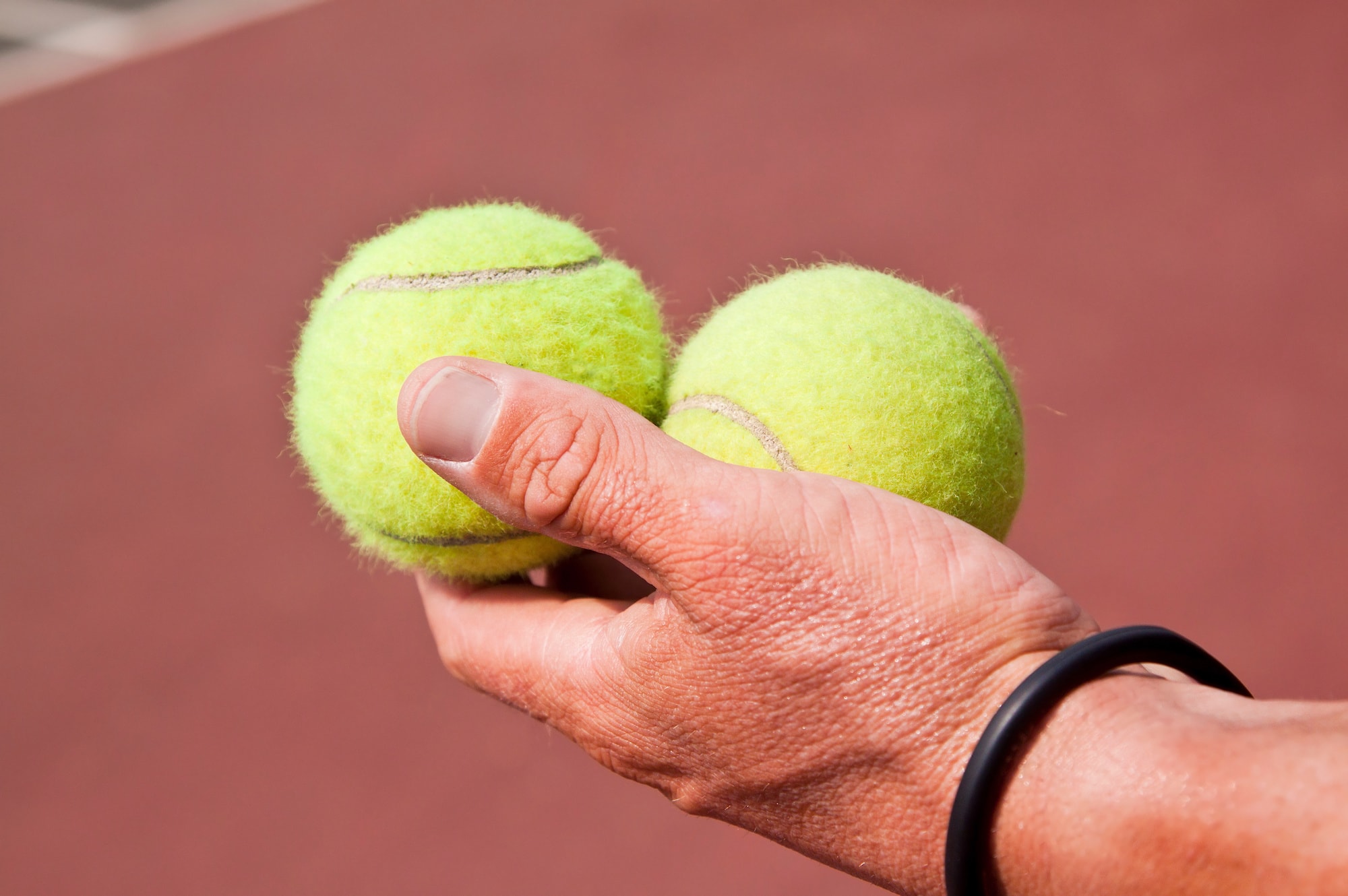Tennis player holding two balls in his hand on court. Hit in the balls