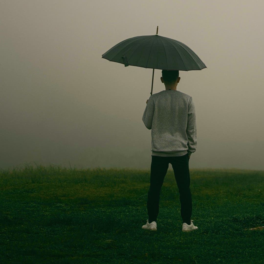 Man holding an umbrella with a dark cloudy sky